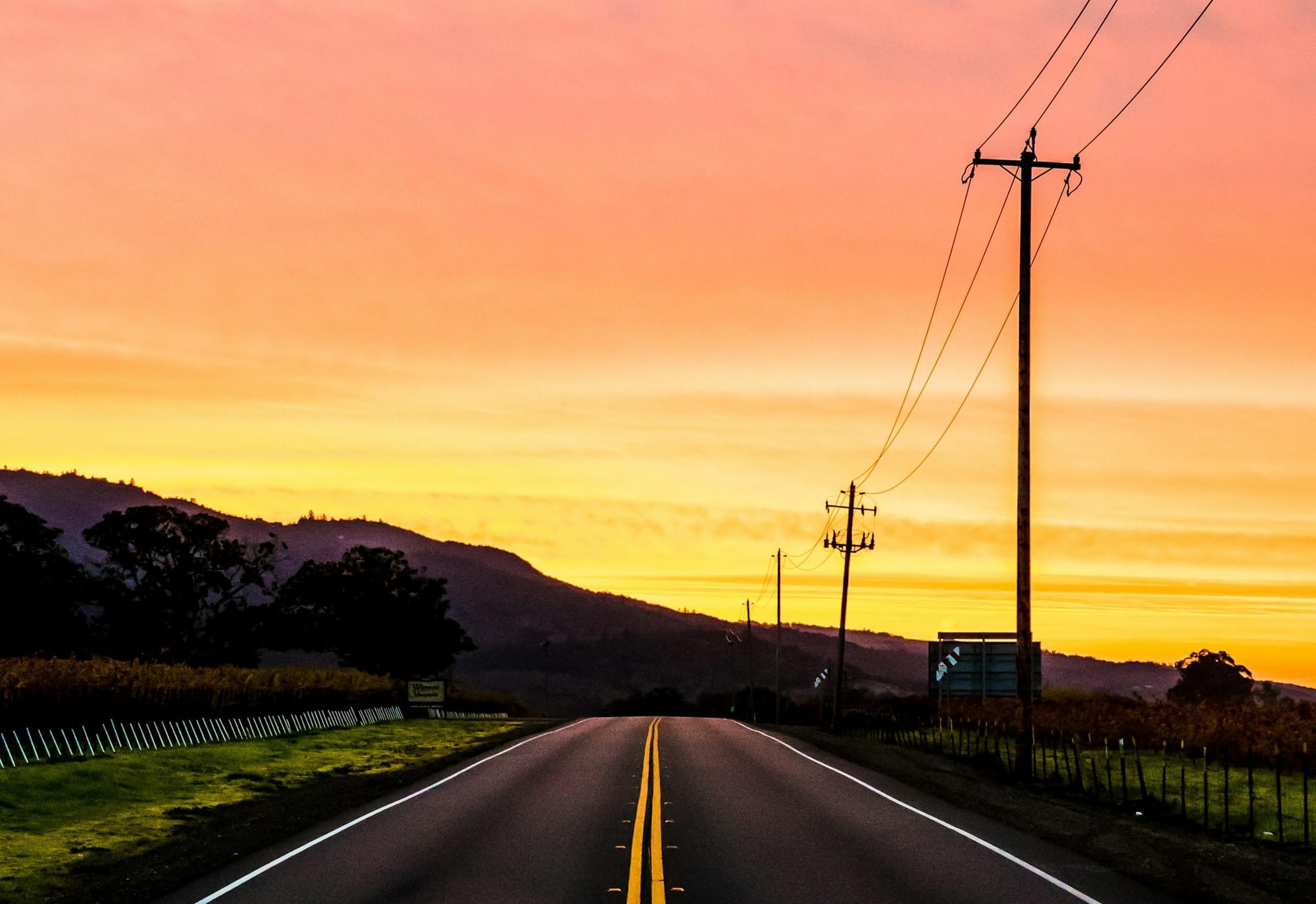 Two lane blacktop road stretches ahead into a colorful sunset