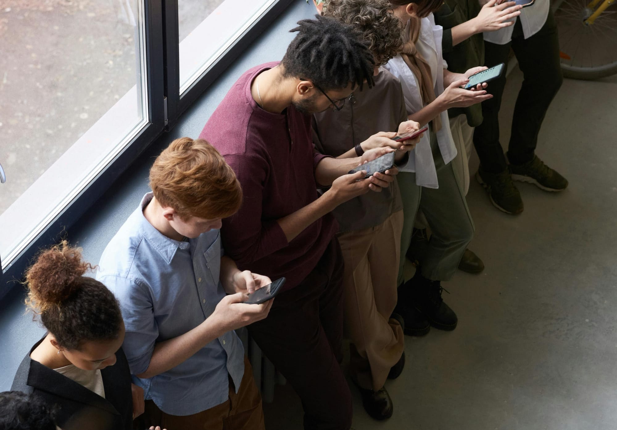 People standing next to each otheer but ignoring each other because each one is reading or typing on their phones.